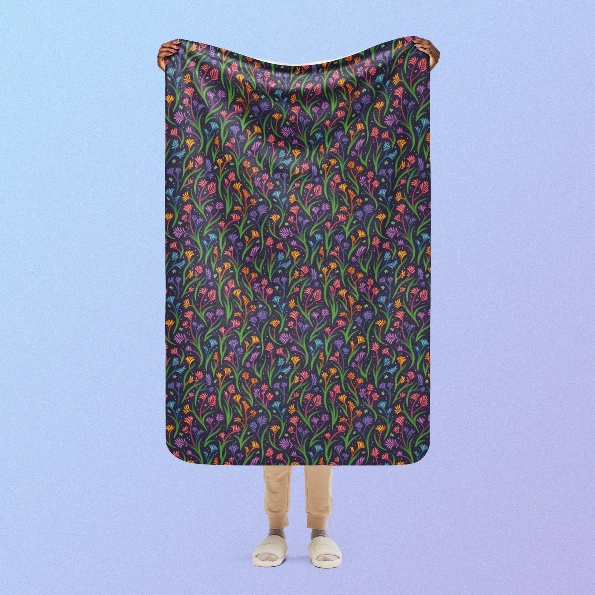 Person holding a rainbow kangaroo paw flower pattern blanket above their head on a blue and purple gradient background.