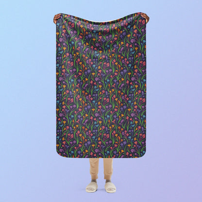 Person holding a rainbow kangaroo paw flower pattern blanket above their head on a blue and purple gradient background.