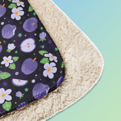 Close up detail of a folded purple apples & blossoms pattern blanket on a blue and green gradient background.