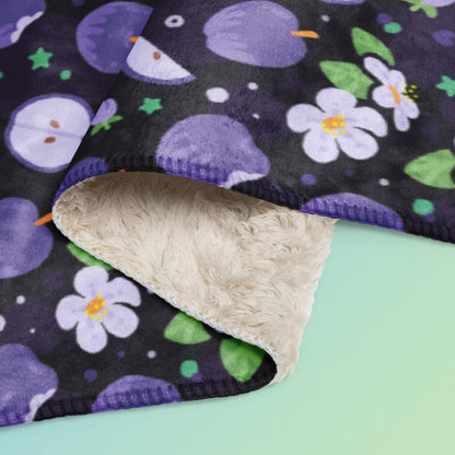 Close up detail of a folded purple apples & blossoms pattern blanket on a blue and green gradient background.