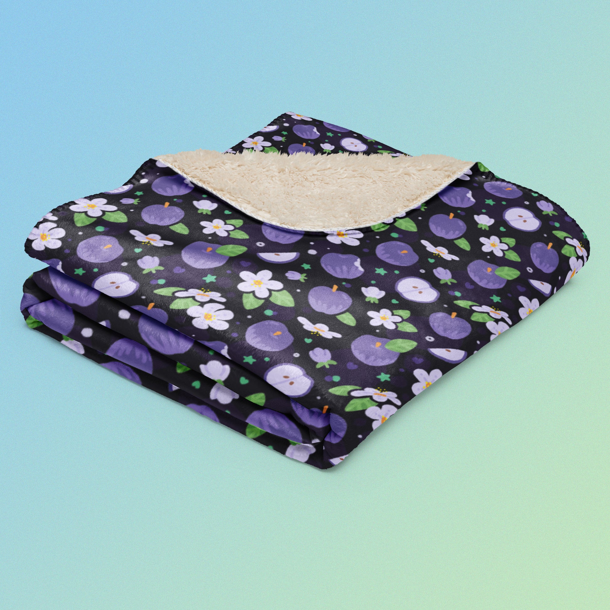A folded purple apples & blossoms pattern blanket on a blue and green gradient background.