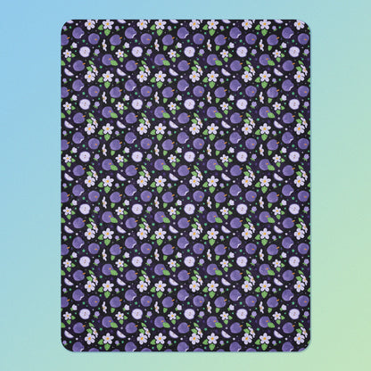 A purple apples & blossoms pattern blanket on a blue and green gradient background.