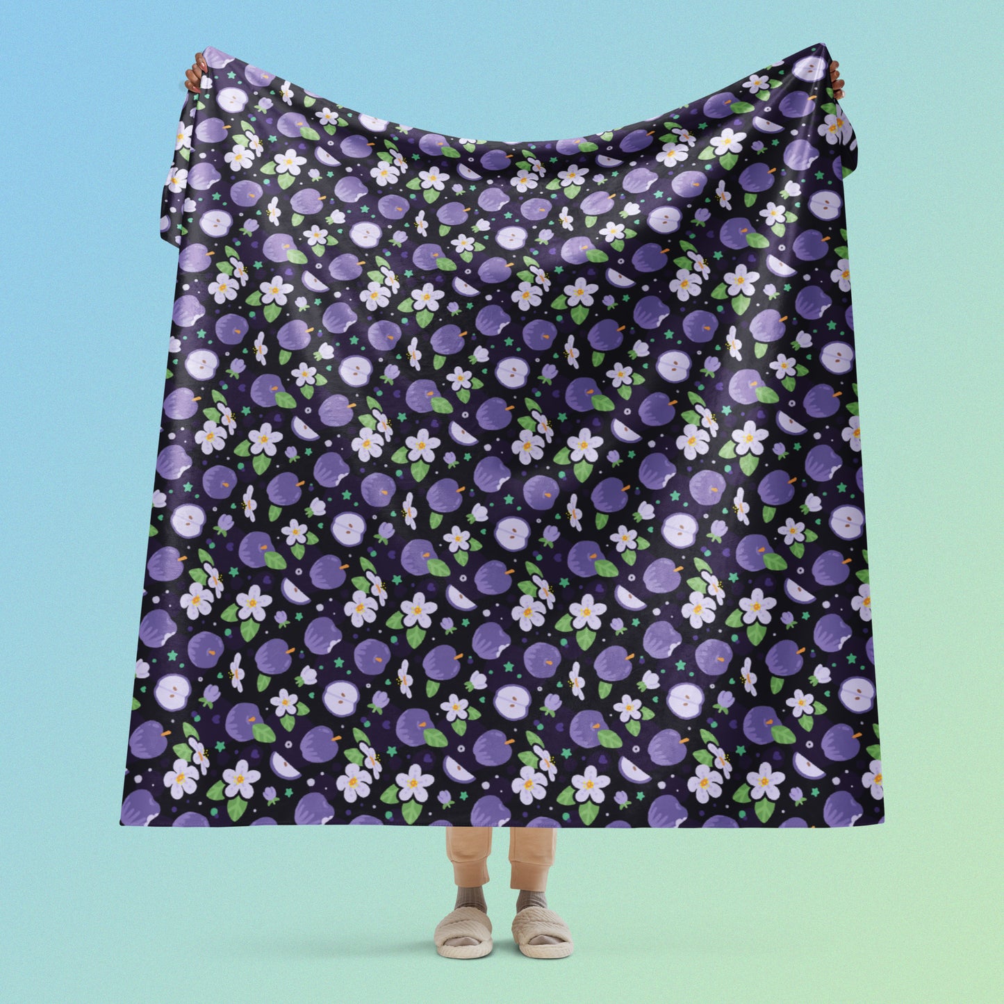 Person holding a purple apples & blossoms pattern blanket above their head on a blue and green gradient background.