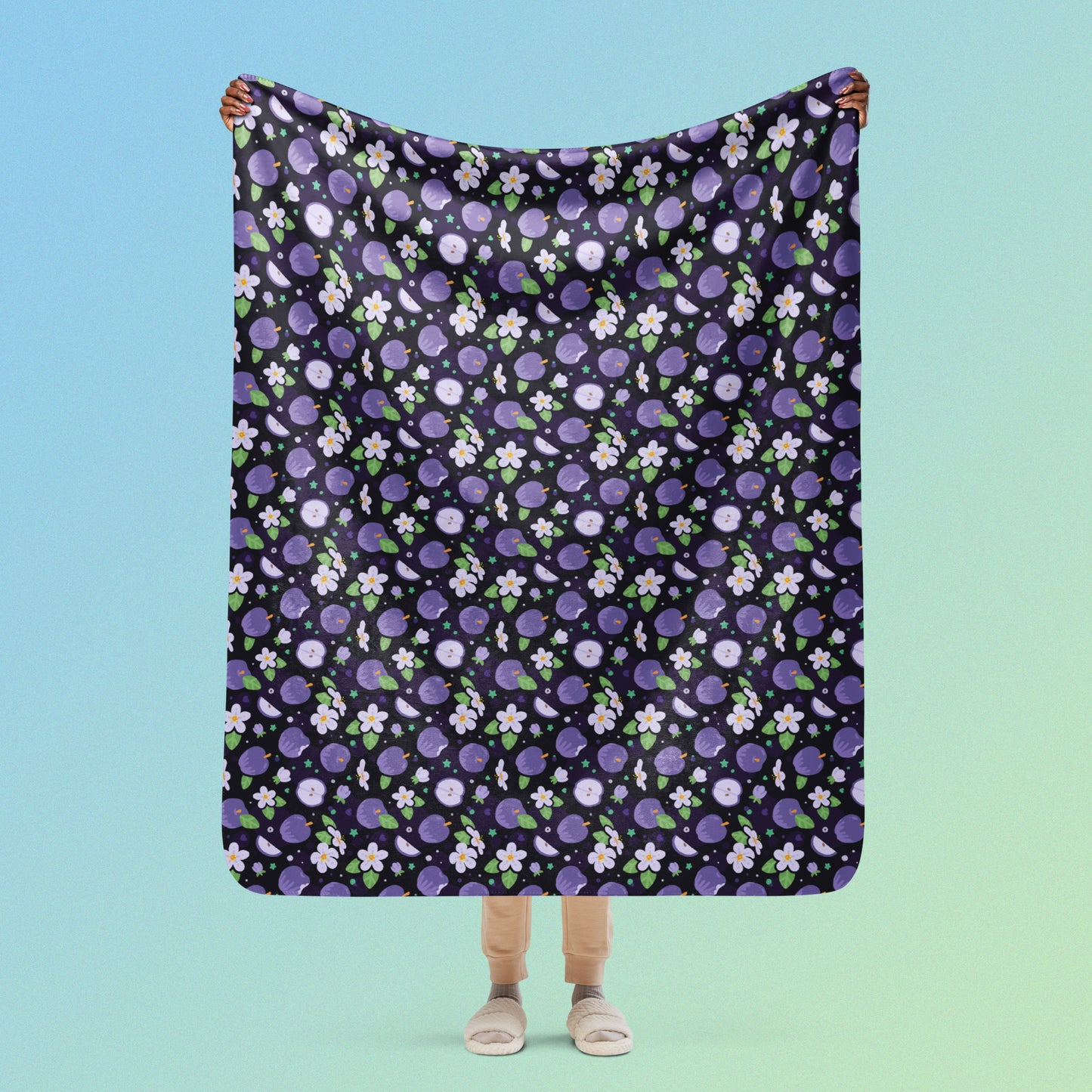 Person holding a purple apples & blossoms pattern blanket above their head on a blue and green gradient background.