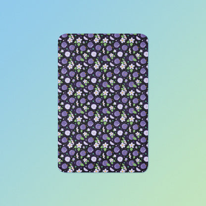 A purple apples & blossoms pattern blanket on a blue and green gradient background.