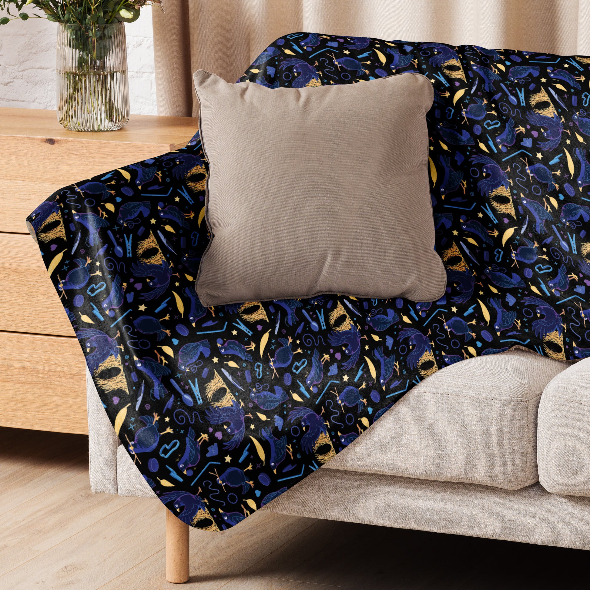 A black, blue, purple and yellow male Aussie satin bowerbird pattern blanket sitting on a beige sofa with a beige pillow on top.
