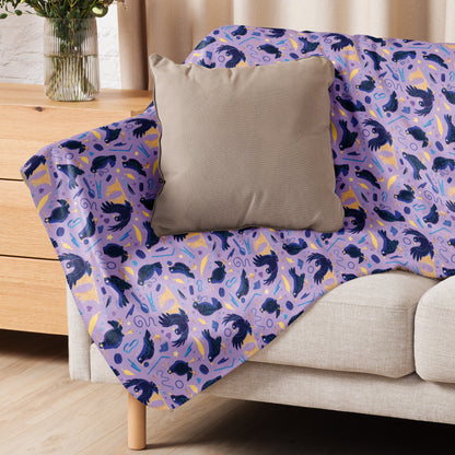 A purple, blue and yellow male Aussie satin bowerbird pattern blanket sitting on a beige sofa with a beige pillow on top.