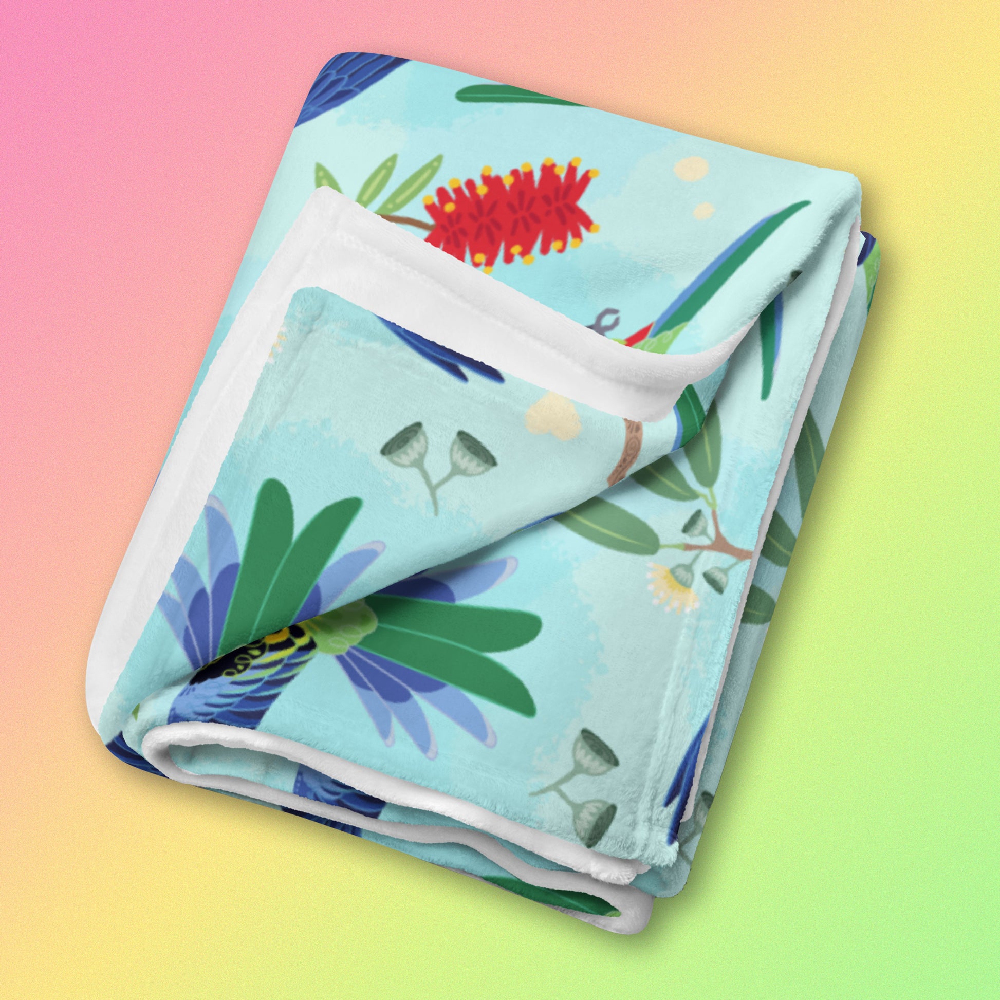 A folded blue, pink and green eastern rosella & native Aussie plant pattern blanket on a pink, yellow and green gradient background.
