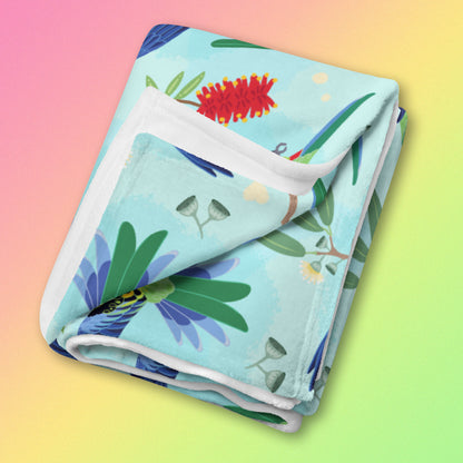 A folded blue, pink and green eastern rosella & native Aussie plant pattern blanket on a pink, yellow and green gradient background.