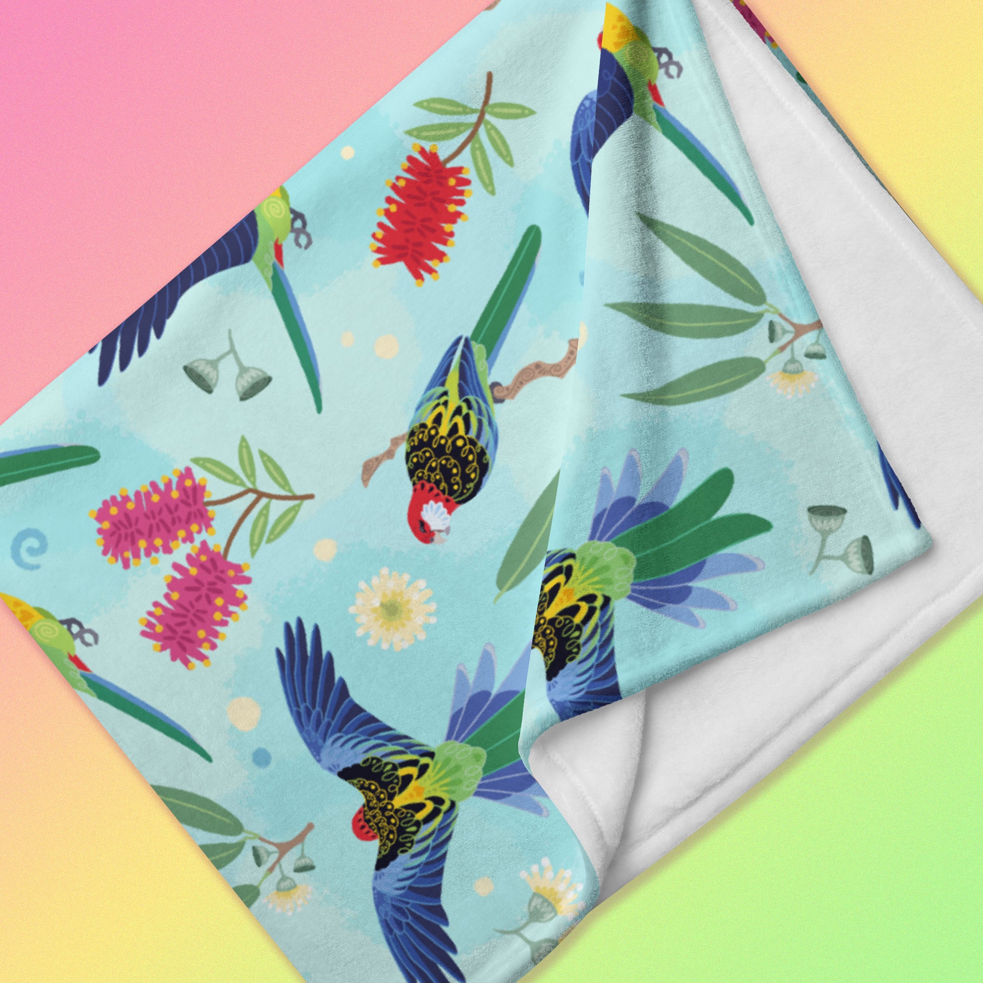 Detailed close up of a folded blue, pink and green eastern rosella & native Aussie plant pattern blanket on a pink, yellow and green gradient background.