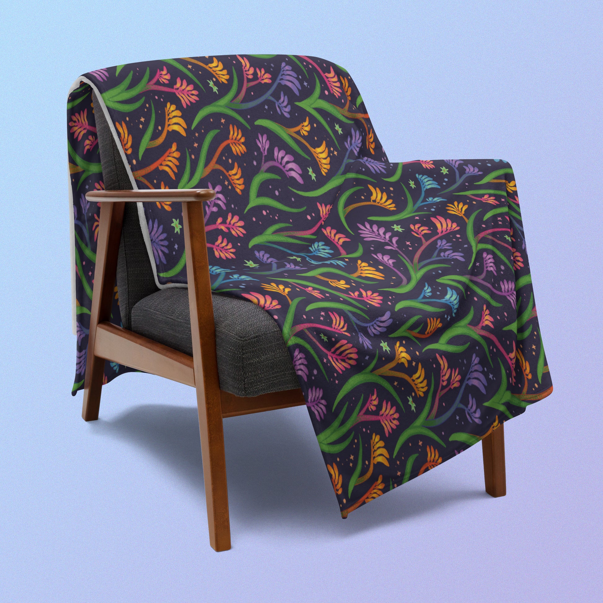 A rainbow kangaroo paw flower pattern blanket draped over a wooden chair on a blue and purple gradient background.