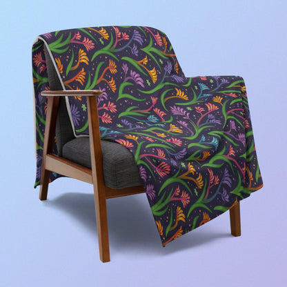 A rainbow kangaroo paw flower pattern blanket draped over a wooden chair on a blue and purple gradient background.