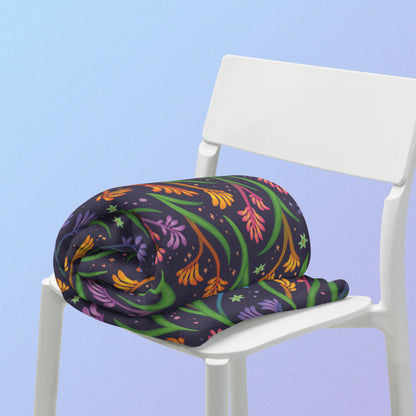 A rolled up rainbow kangaroo paw flower pattern blanket sitting on a white chair on a blue and purple gradient background.