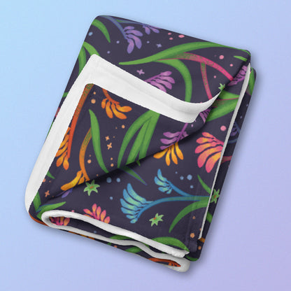 A folded rainbow kangaroo paw flower pattern blanket on a blue and purple gradient background.