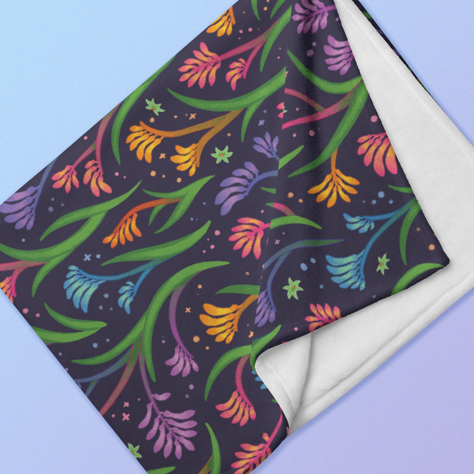 Close up detail of a folded rainbow kangaroo paw flower pattern blanket on a blue and purple gradient background.