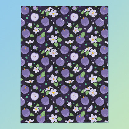 A purple apples & blossoms pattern blanket on a blue and green gradient background.