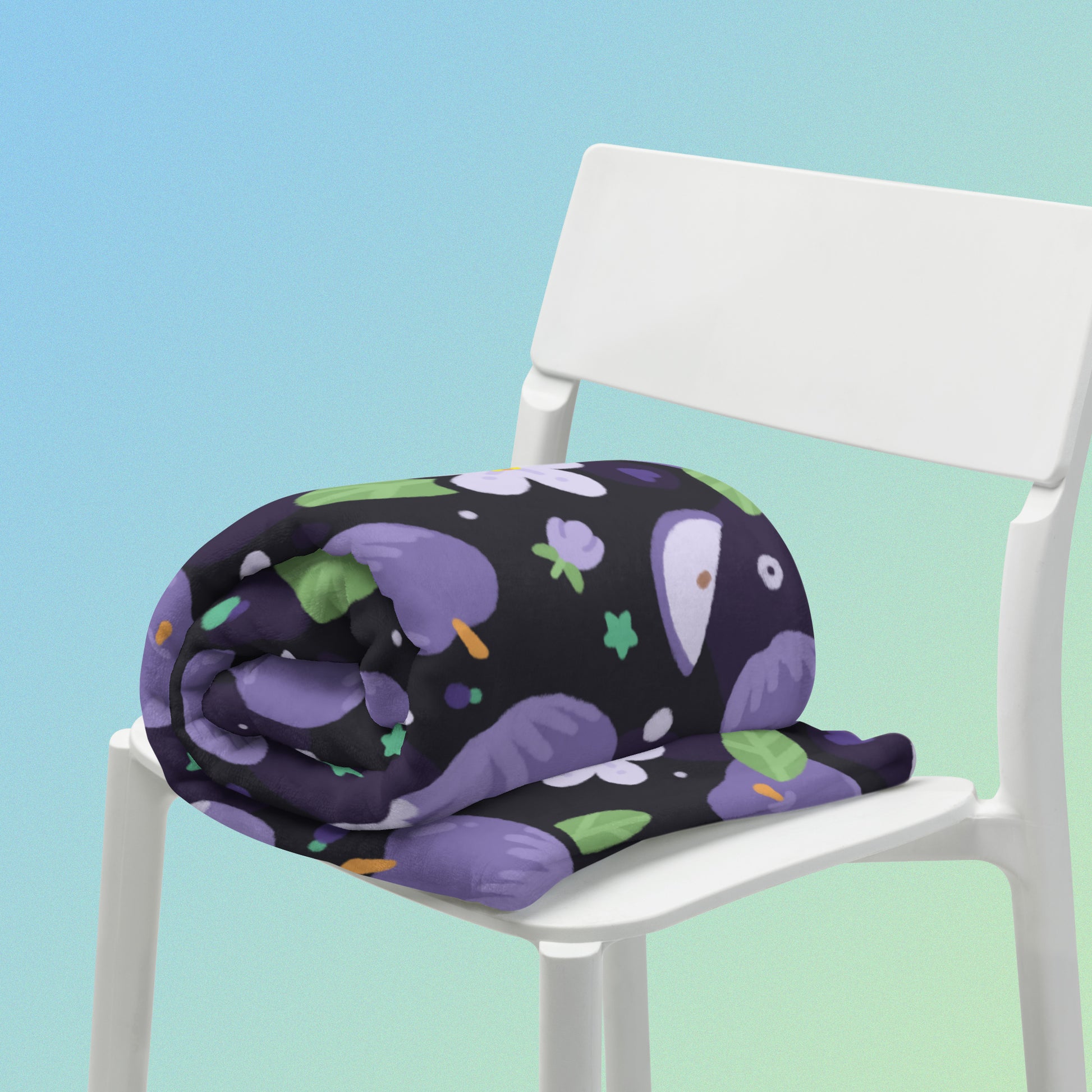 A rolled up purple apples & blossoms pattern blanket sitting on a white chair on a blue and green gradient background.