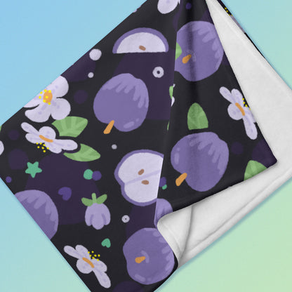 Close up detail of a folded purple apples & blossoms pattern blanket on a blue and green gradient background.