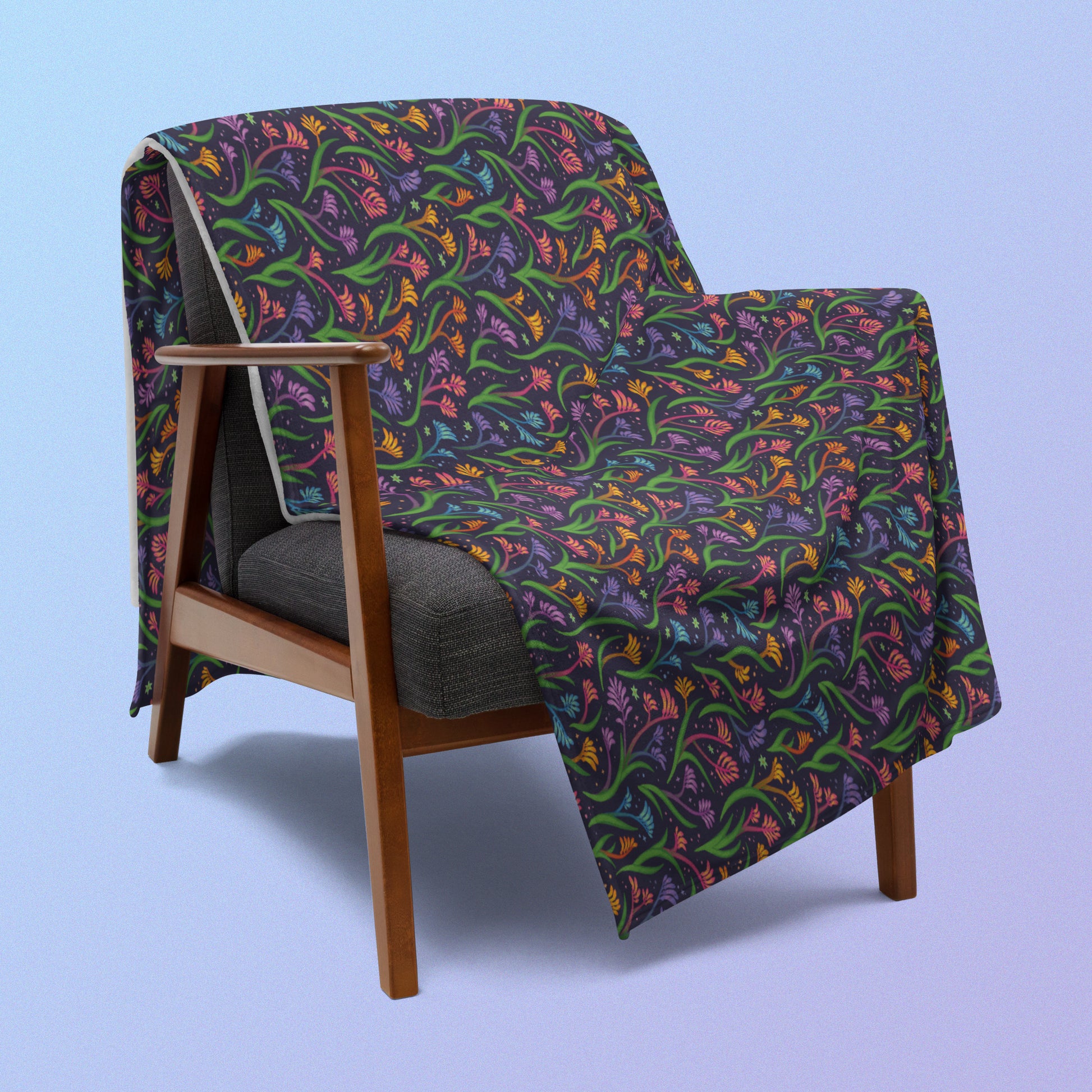 A rainbow kangaroo paw flower pattern blanket draped over a wooden chair on a blue and purple gradient background.