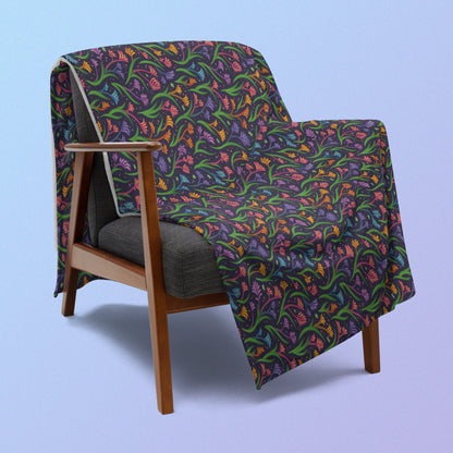 A rainbow kangaroo paw flower pattern blanket draped over a wooden chair on a blue and purple gradient background.