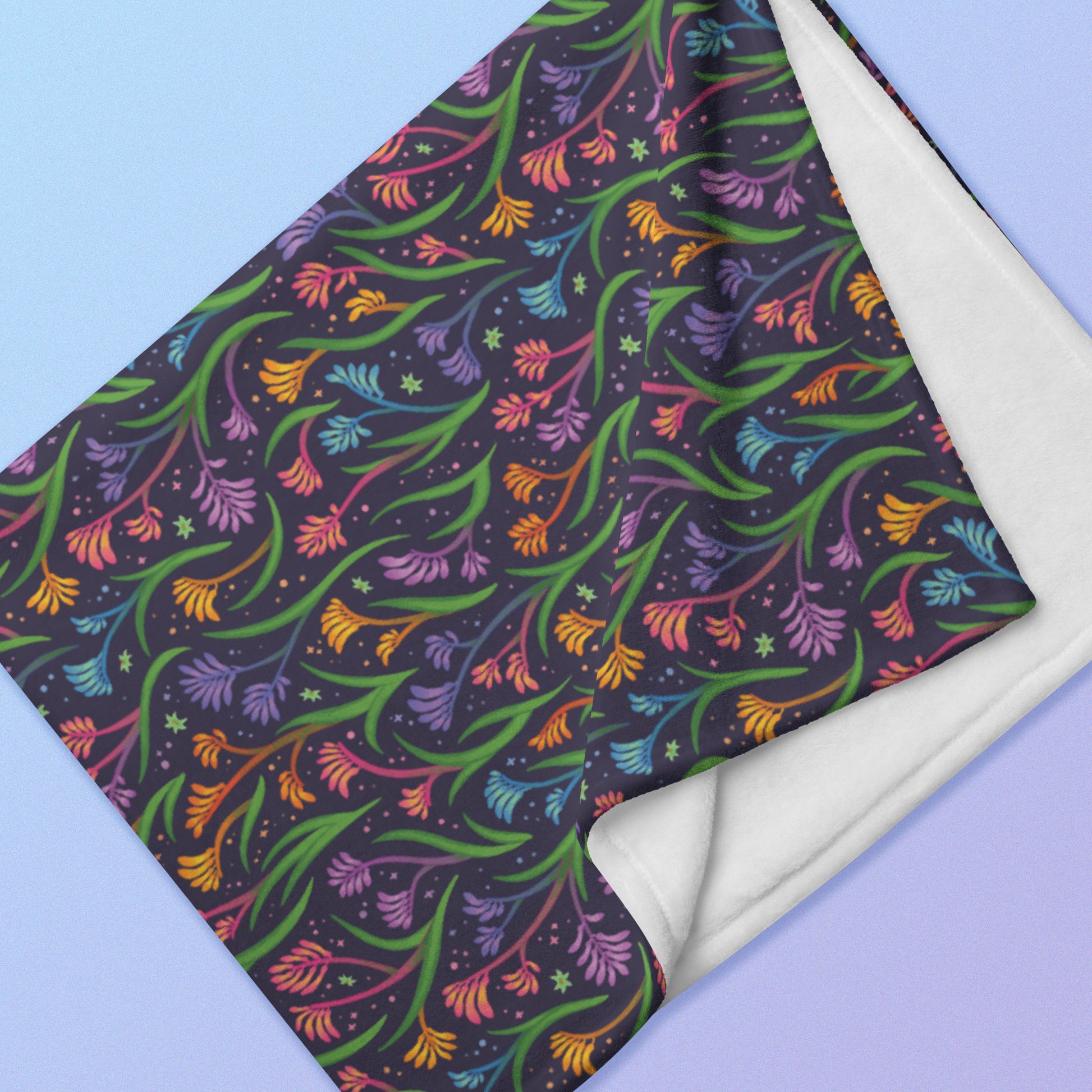 Close up detail of a folded rainbow kangaroo paw flower pattern blanket on a blue and purple gradient background.