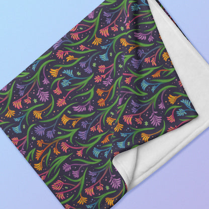 Close up detail of a folded rainbow kangaroo paw flower pattern blanket on a blue and purple gradient background.