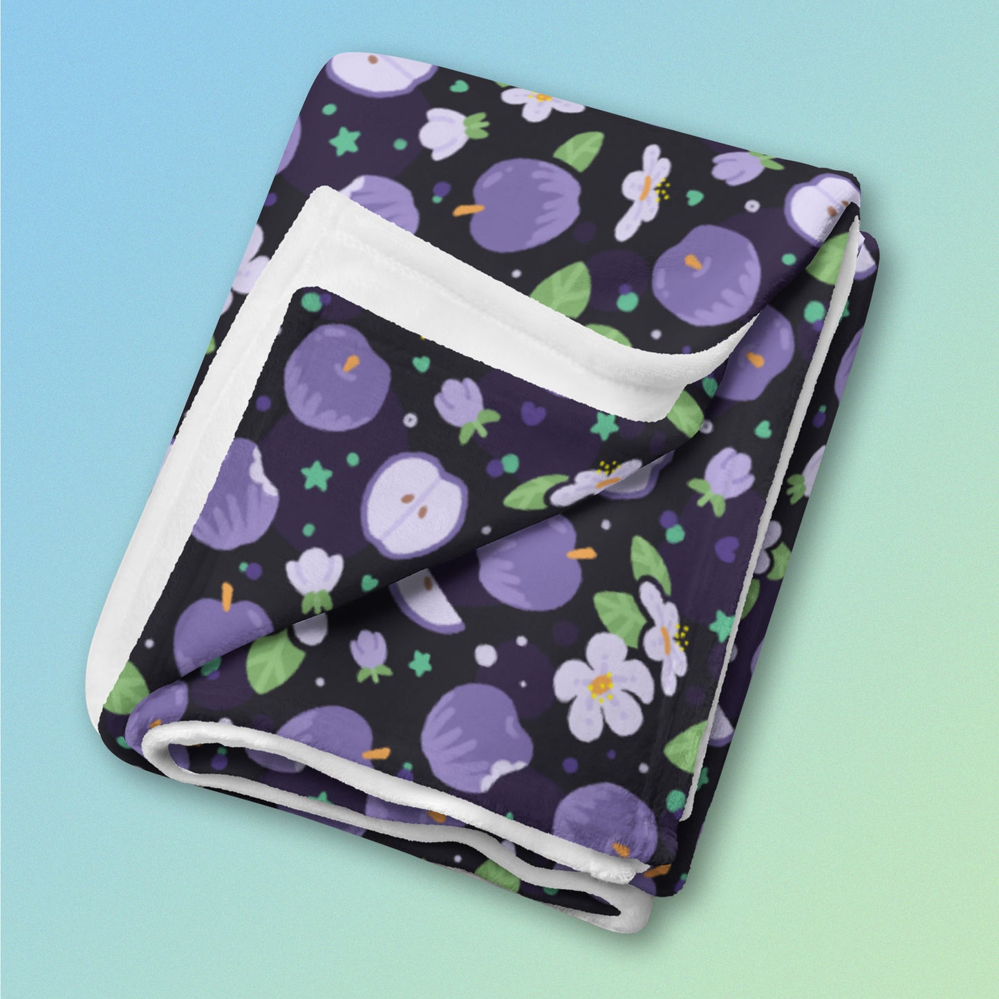 A folded purple apples & blossoms pattern blanket on a blue and green gradient background.