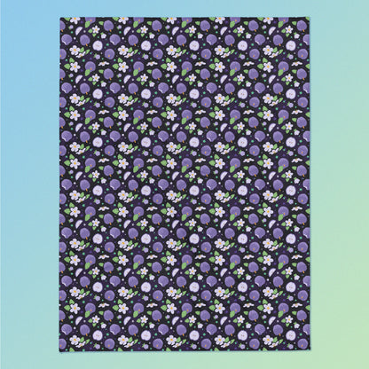 A purple apples & blossoms pattern blanket on a blue and green gradient background.