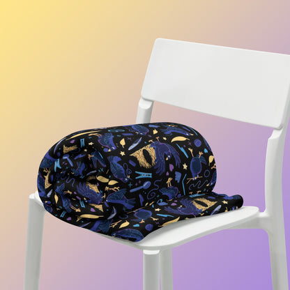 A rolled up black, blue, purple and yellow male Aussie satin bowerbird pattern blanket sitting on a white chair on a yellow and purple gradient background.