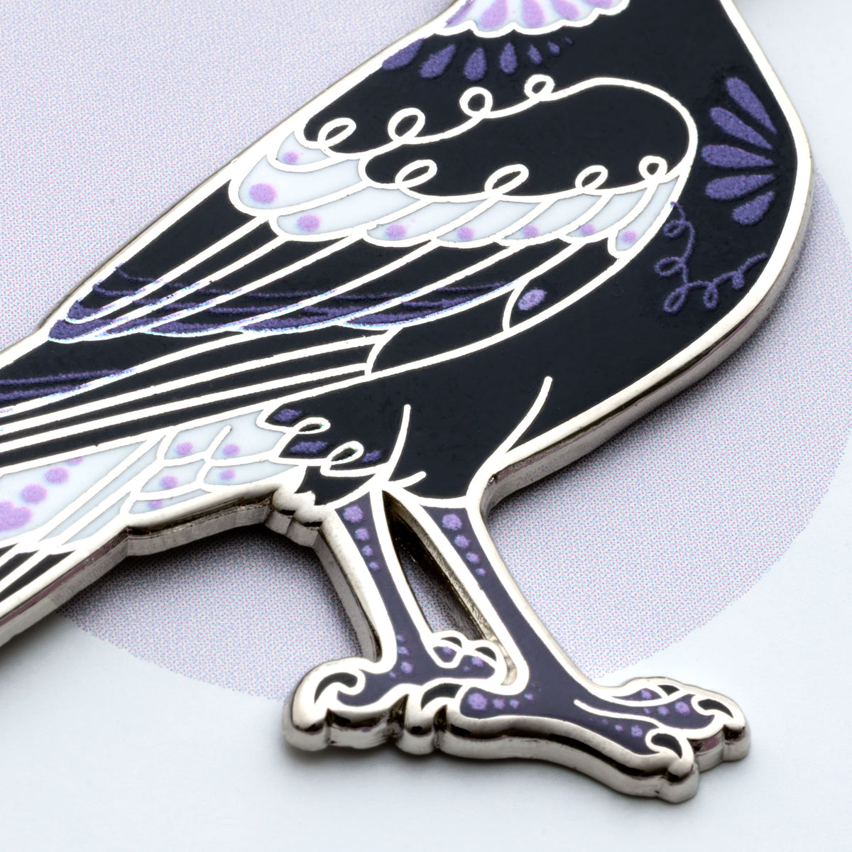 Close up on the body of a nickel-plated Australian magpie hard enamel pin on a 'Feather Creates' branded backing card sitting on an angle on a purple background.