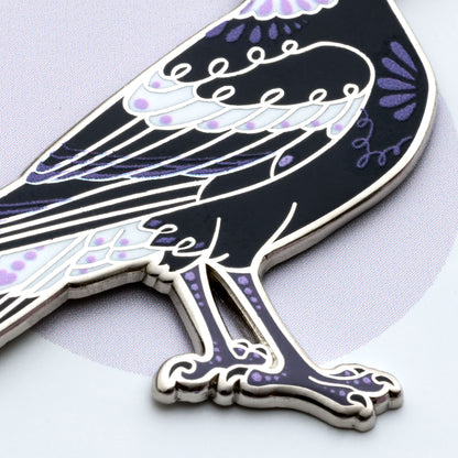 Close up on the body of a nickel-plated Australian magpie hard enamel pin on a 'Feather Creates' branded backing card sitting on an angle on a purple background.