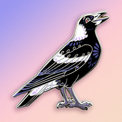 A nickel-plated Australian magpie hard enamel pin on a blue, purple and pink gradient background.