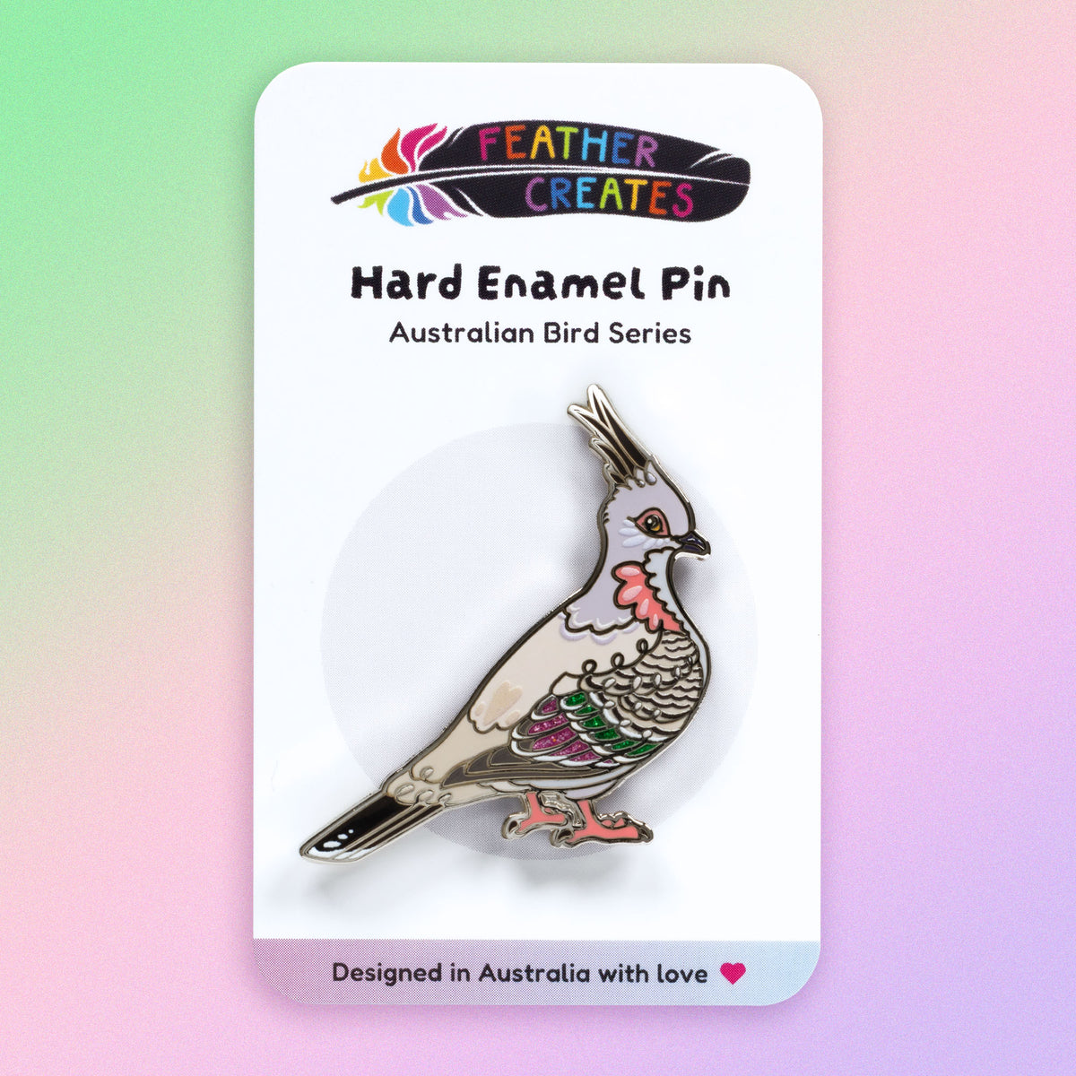 A nickel-plated crested pigeon hard enamel pin sitting on a 'Feather Creates' branded backing card on a green, purple and pink gradient background.