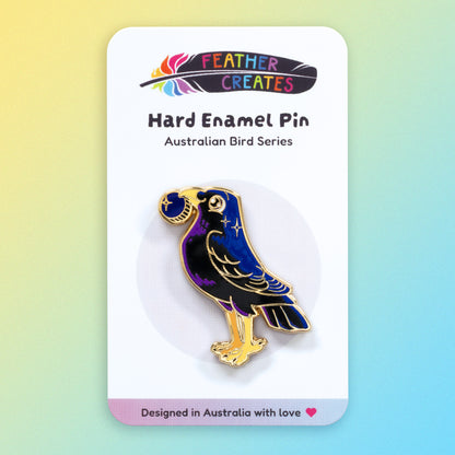 A gold-plated satin bowerbird hard enamel pin sitting on a 'Feather Creates' branded backing card on a blue and yellow gradient background.