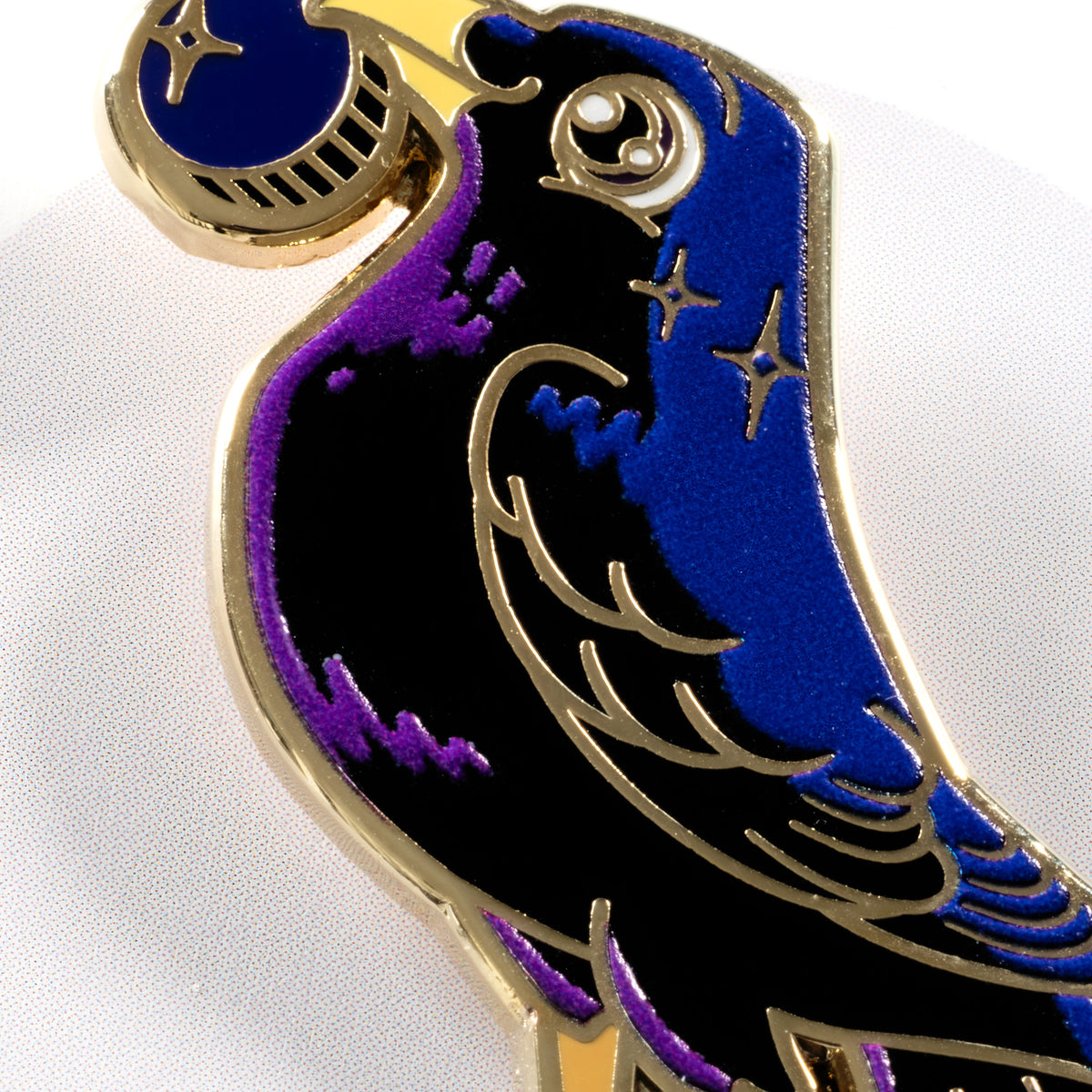 Closeup on the face and body of a  gold-plated satin bowerbird hard enamel pin on a white background.