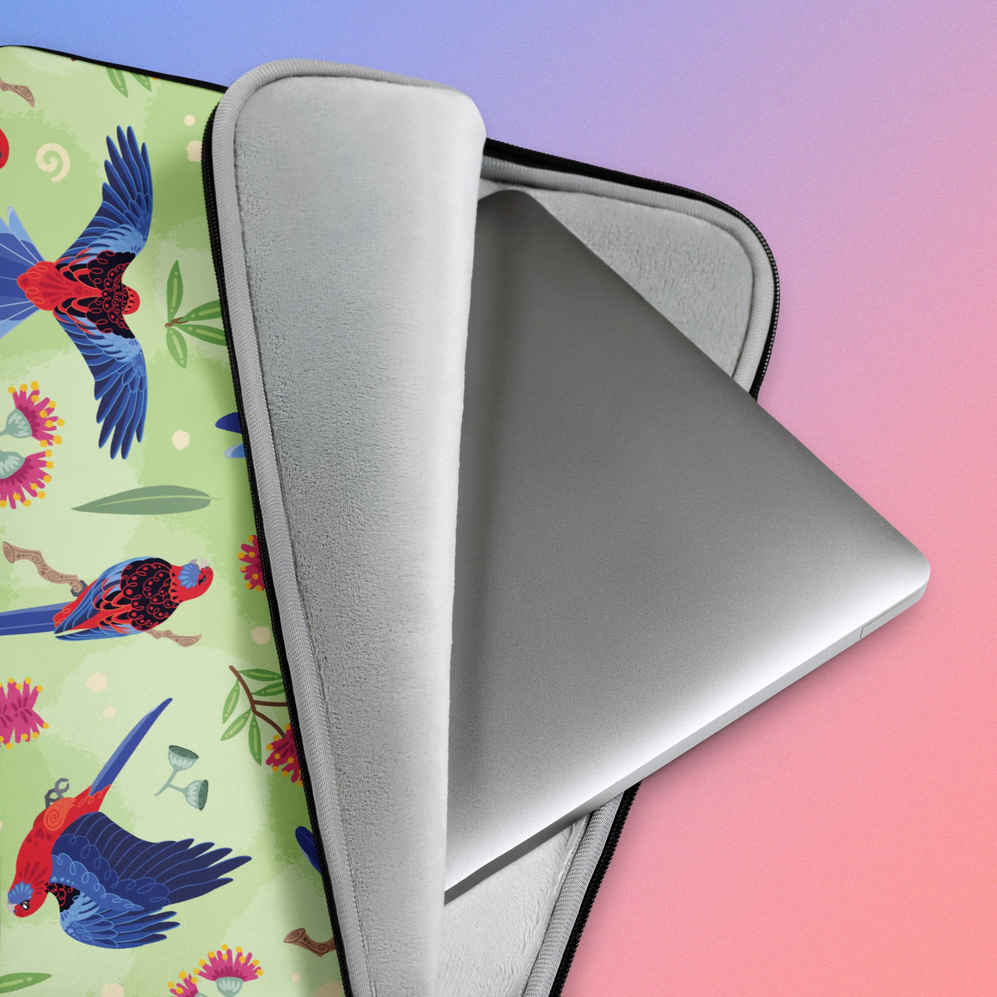 Close up detail of a laptop sitting in a laptop sleeve with a colourful green, red, blue and pink crimson rosella pattern on a pink and blue gradient background.