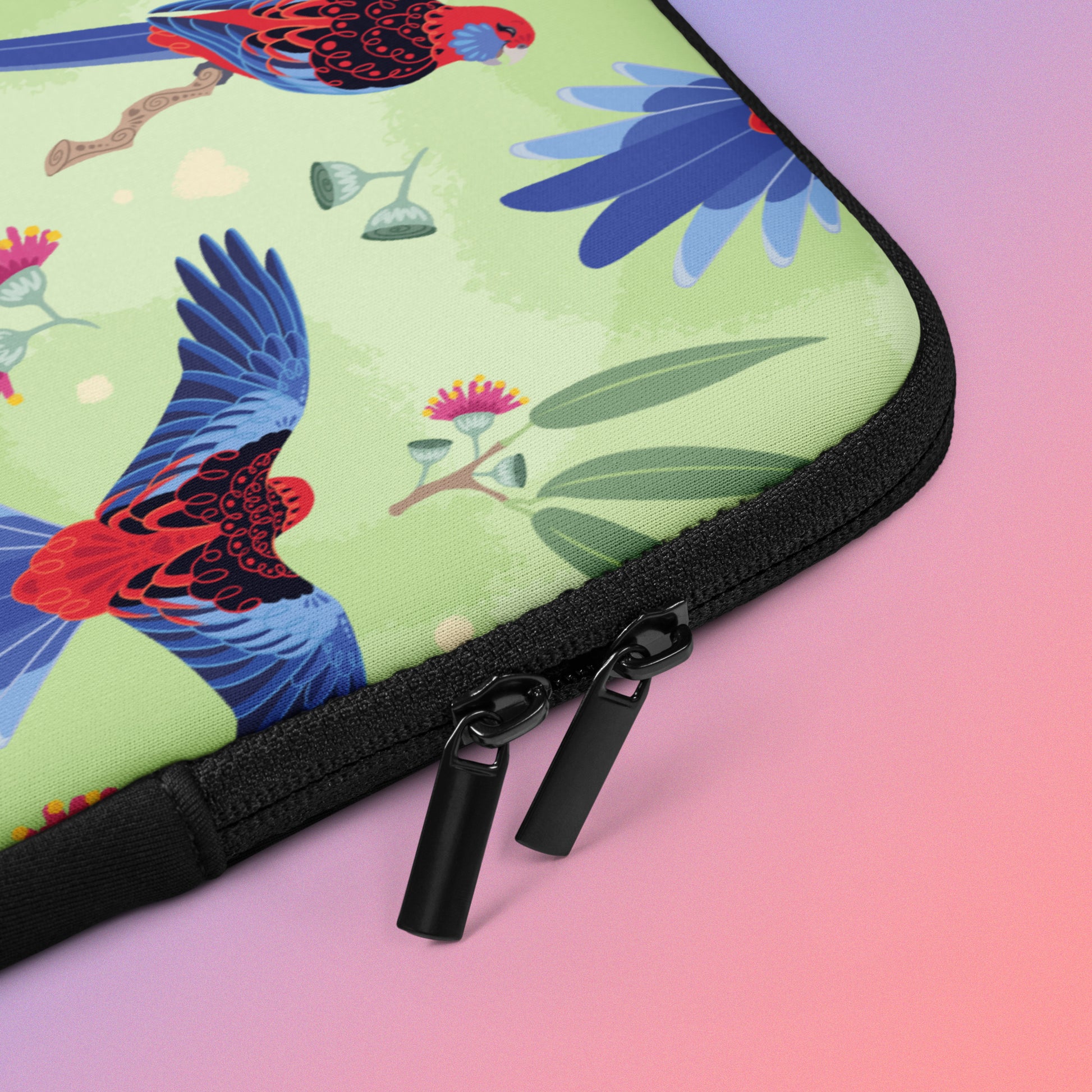 Close up detail of a laptop sleeve with a colourful green, red, blue and pink crimson rosella pattern on a pink and blue gradient background.