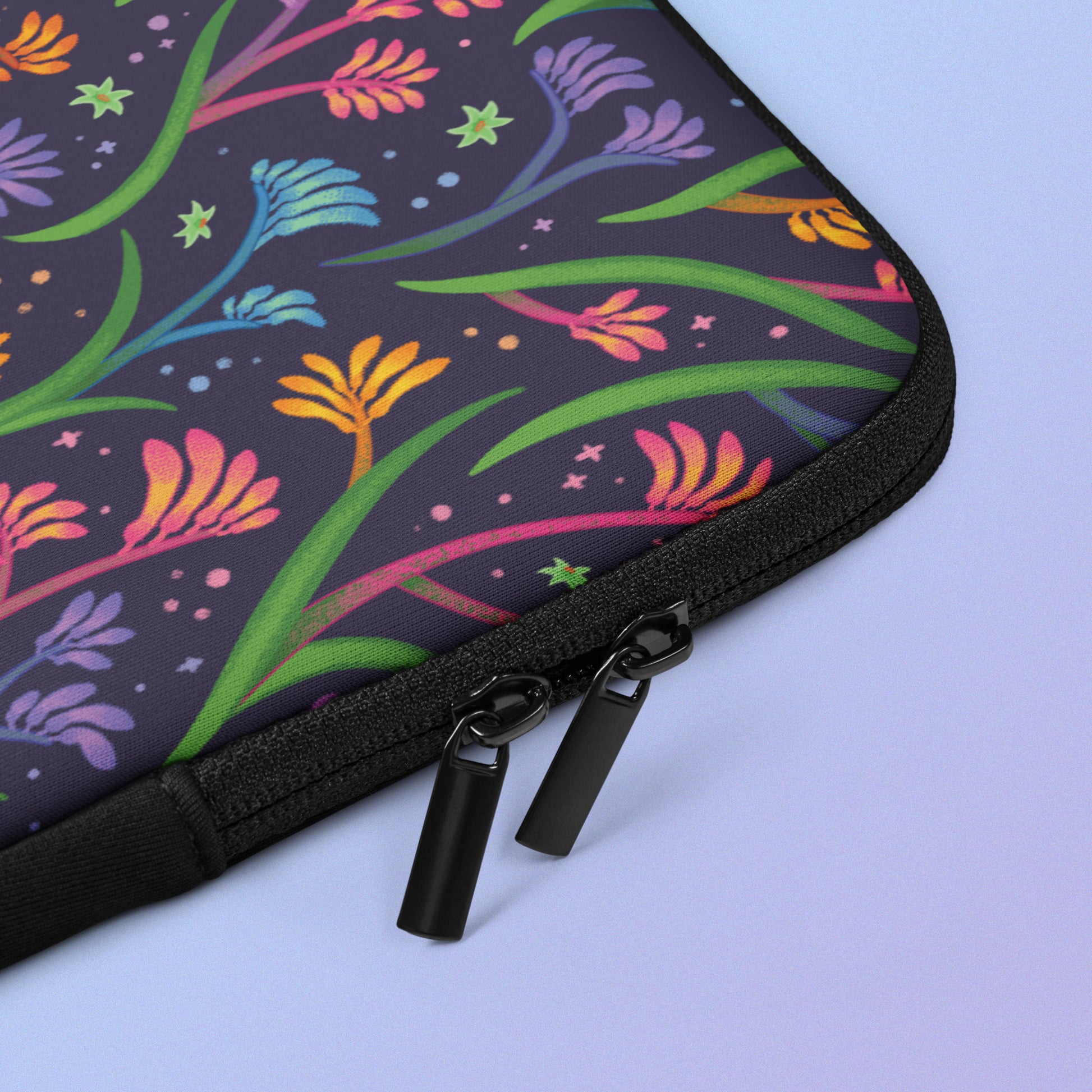 Close up detail of laptop sleeve with a colourful rainbow kangaroo paw flower pattern on a blue and purple gradient background.