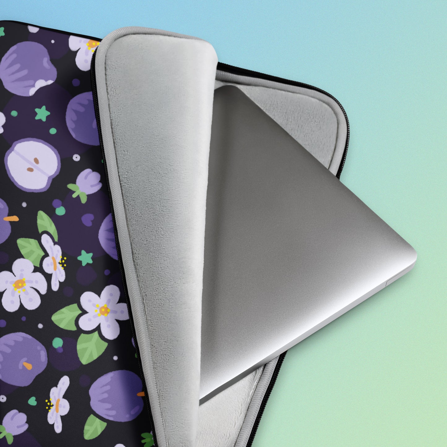 Close up detail of a laptop sitting inside a laptop sleeve with a colourful purple apples and apple blossoms pattern on a blue and green gradient background.