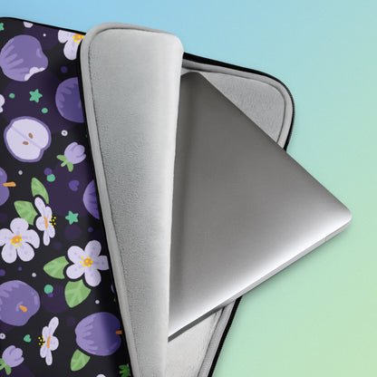 Close up detail of a laptop sitting inside a laptop sleeve with a colourful purple apples and apple blossoms pattern on a blue and green gradient background.