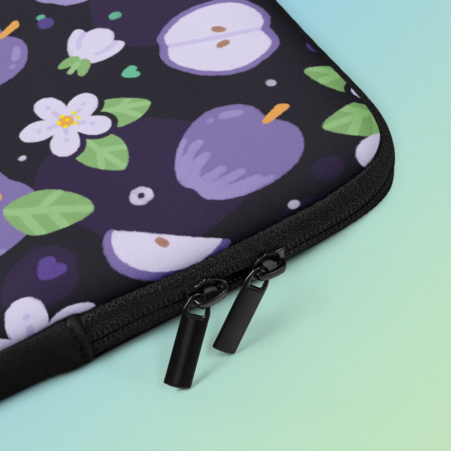 Close up detail of a laptop sleeve with a colourful purple apples and apple blossoms pattern on a blue and green gradient background.