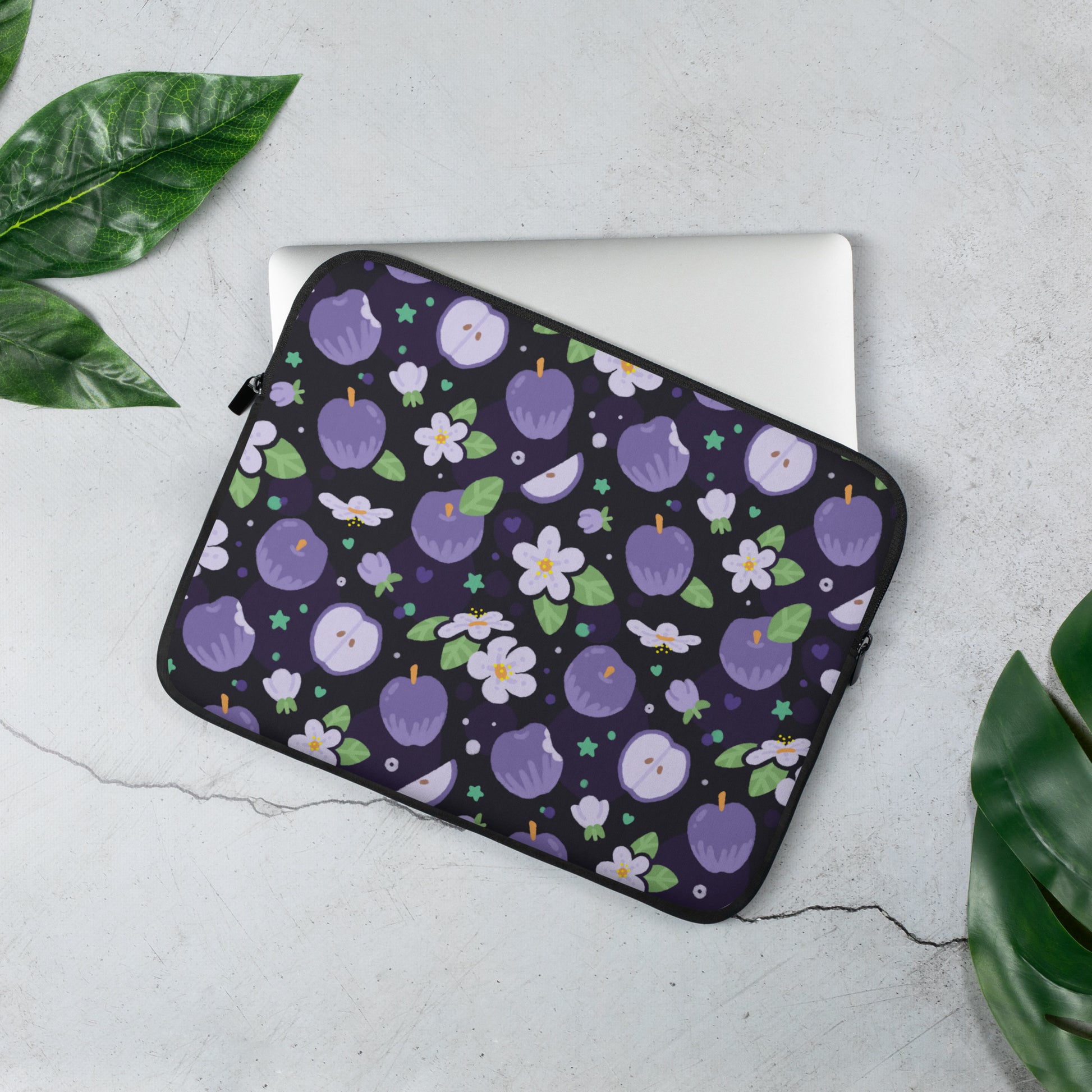 Laptop sleeve with a colourful purple apples and apple blossoms pattern  sitting on a marble table surrounded by leaves.