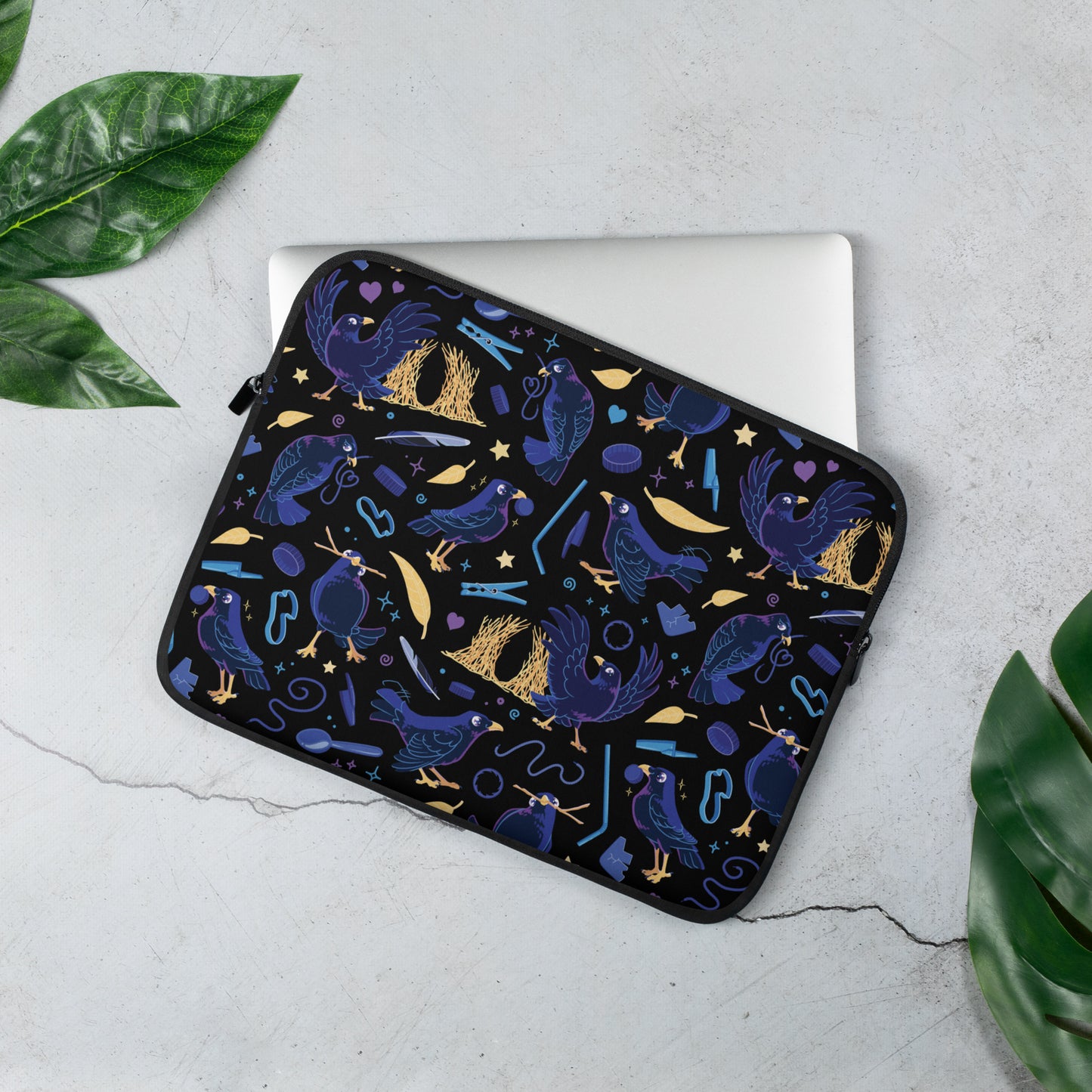Laptop sleeve with a colourful purple, blue and yellow satin bowerbird pattern sitting on a marble table surrounded by leaves.