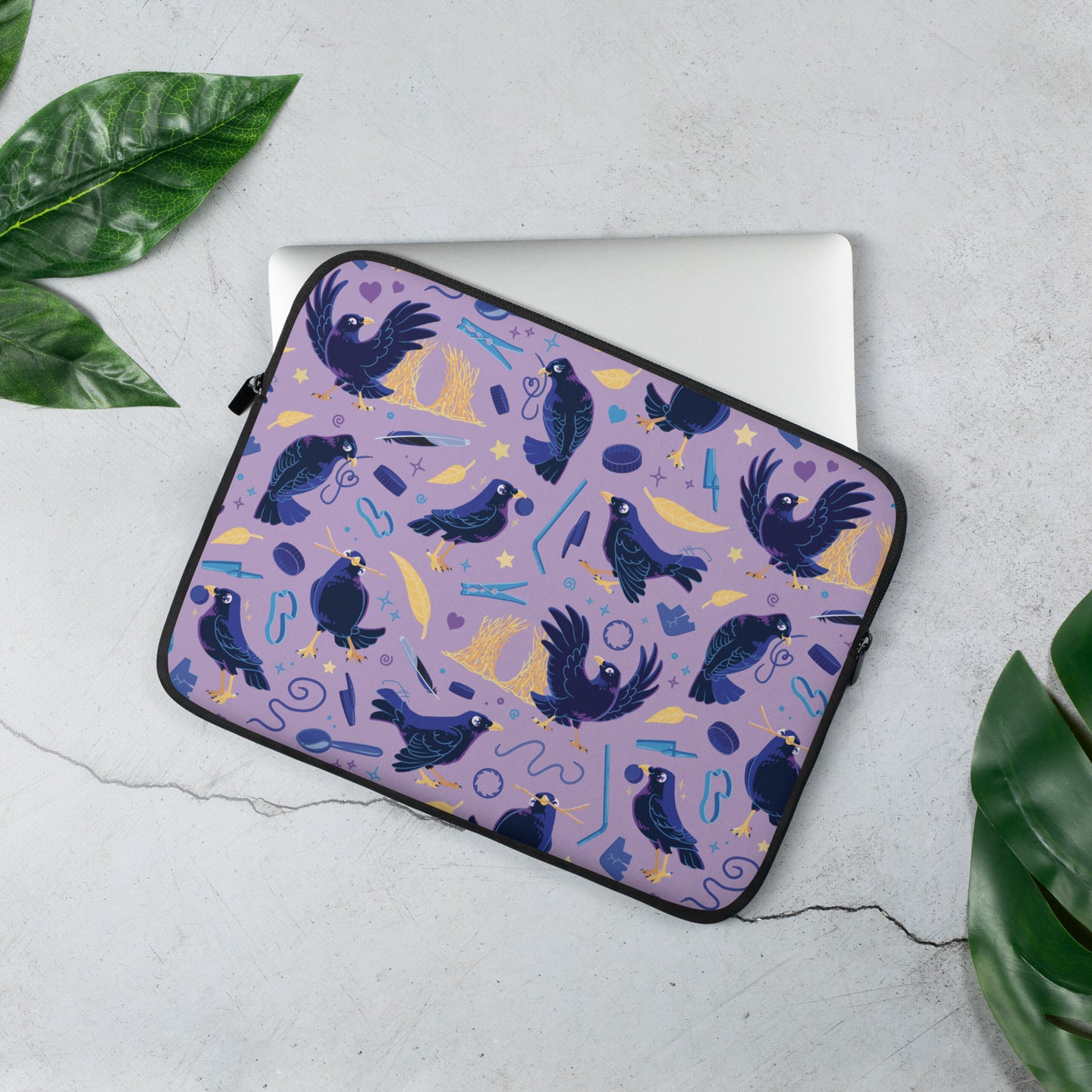 Laptop sitting in a laptop sleeve with a colourful purple, blue and yellow satin bowerbird pattern sitting on a marble table surrounded by leaves.