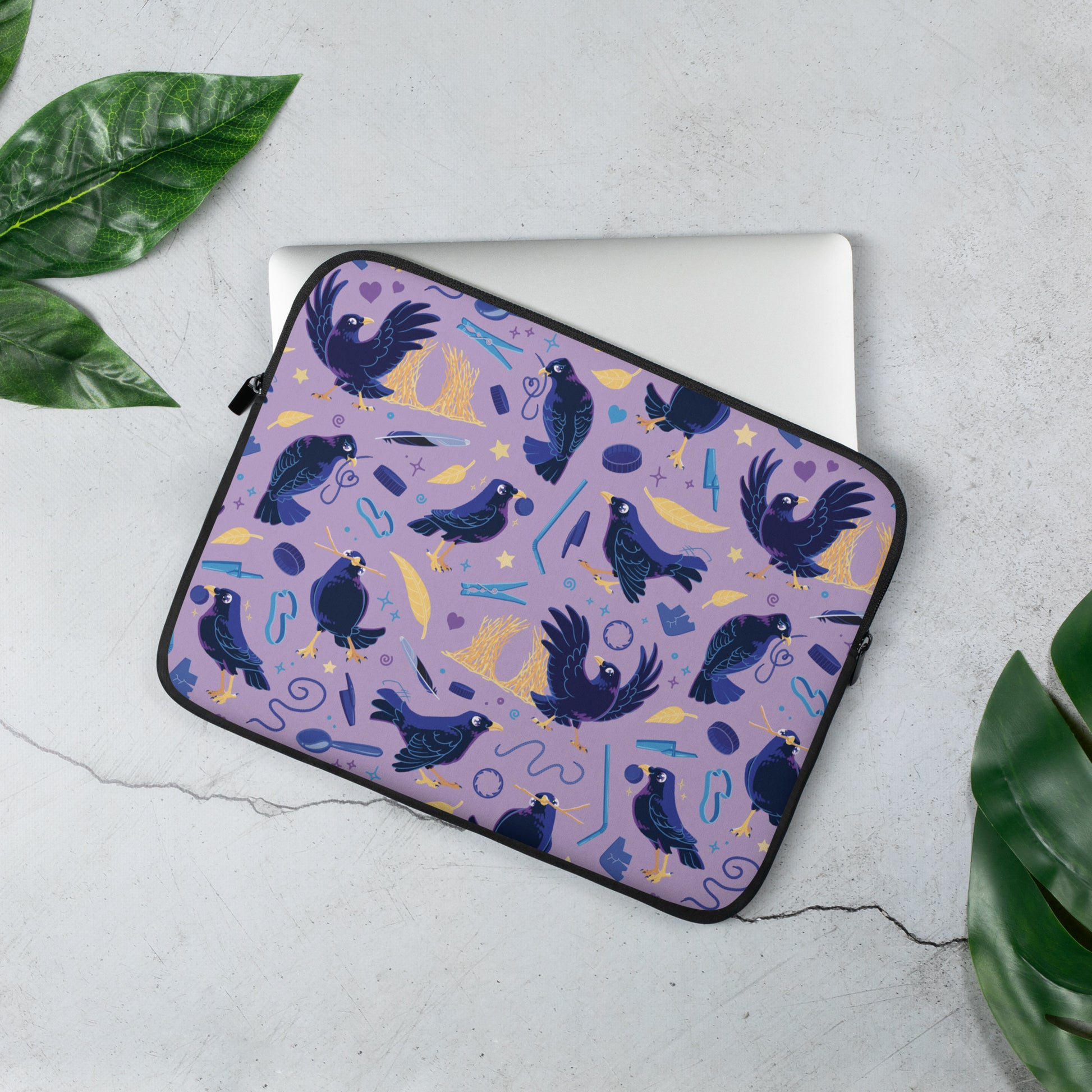 Laptop sitting in a laptop sleeve with a colourful purple, blue and yellow satin bowerbird pattern sitting on a marble table surrounded by leaves.