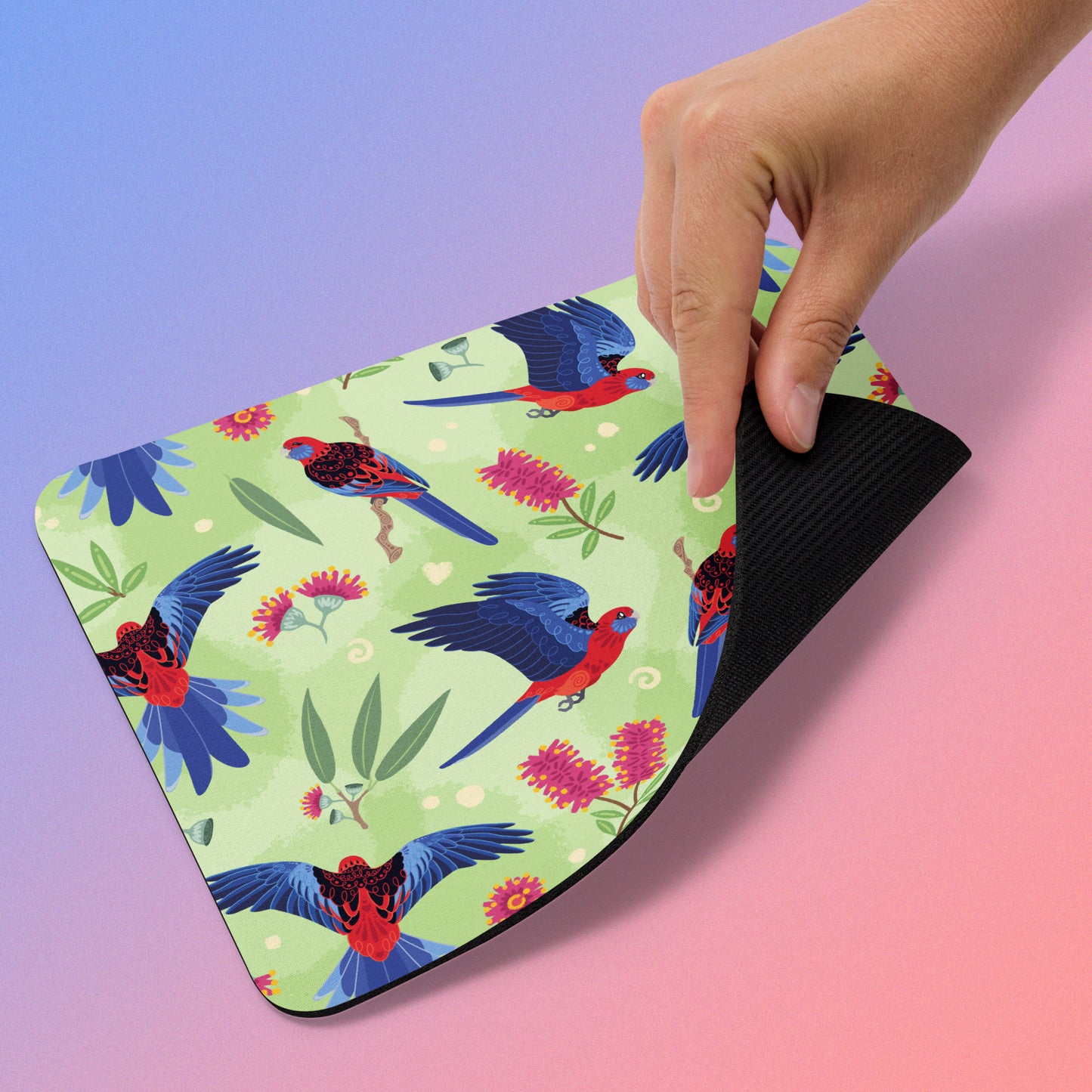 Mouse pad with a crimson rosella parrot design held by a hand on a blue-pink gradient background