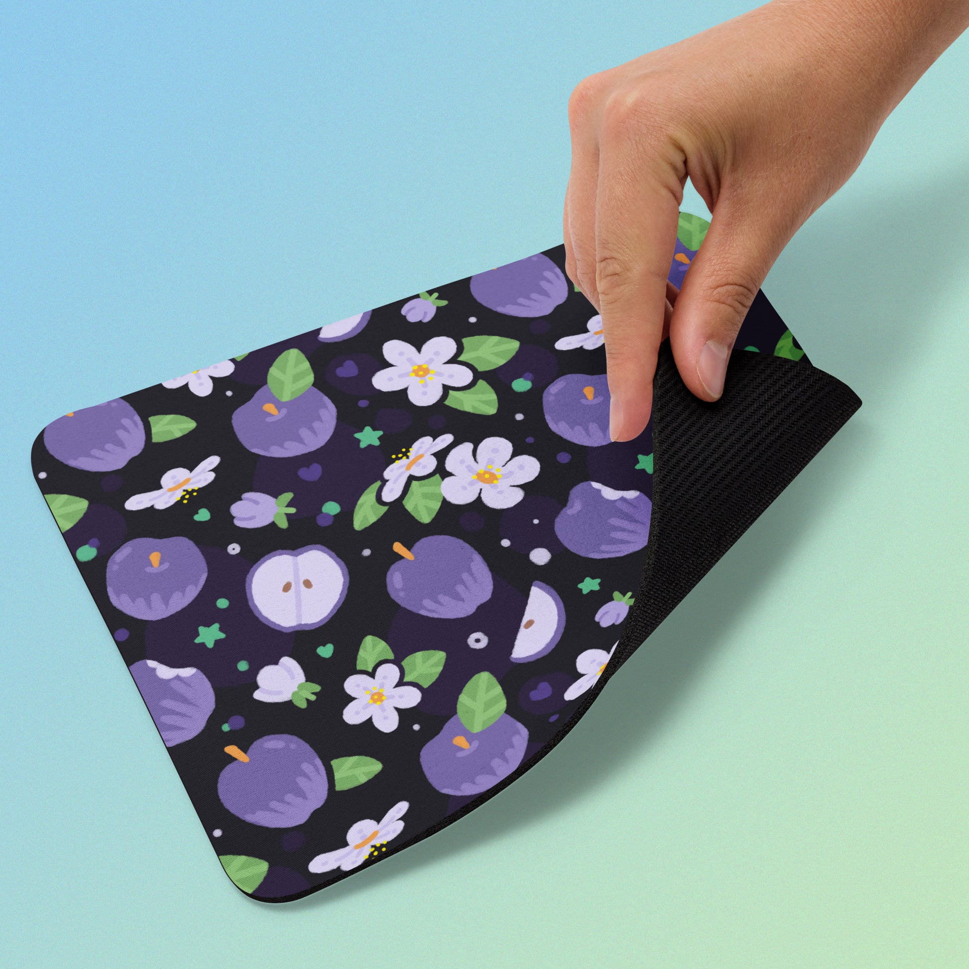 Mouse pad with purple fruit and flower pattern held by a hand on a blue and green gradient background