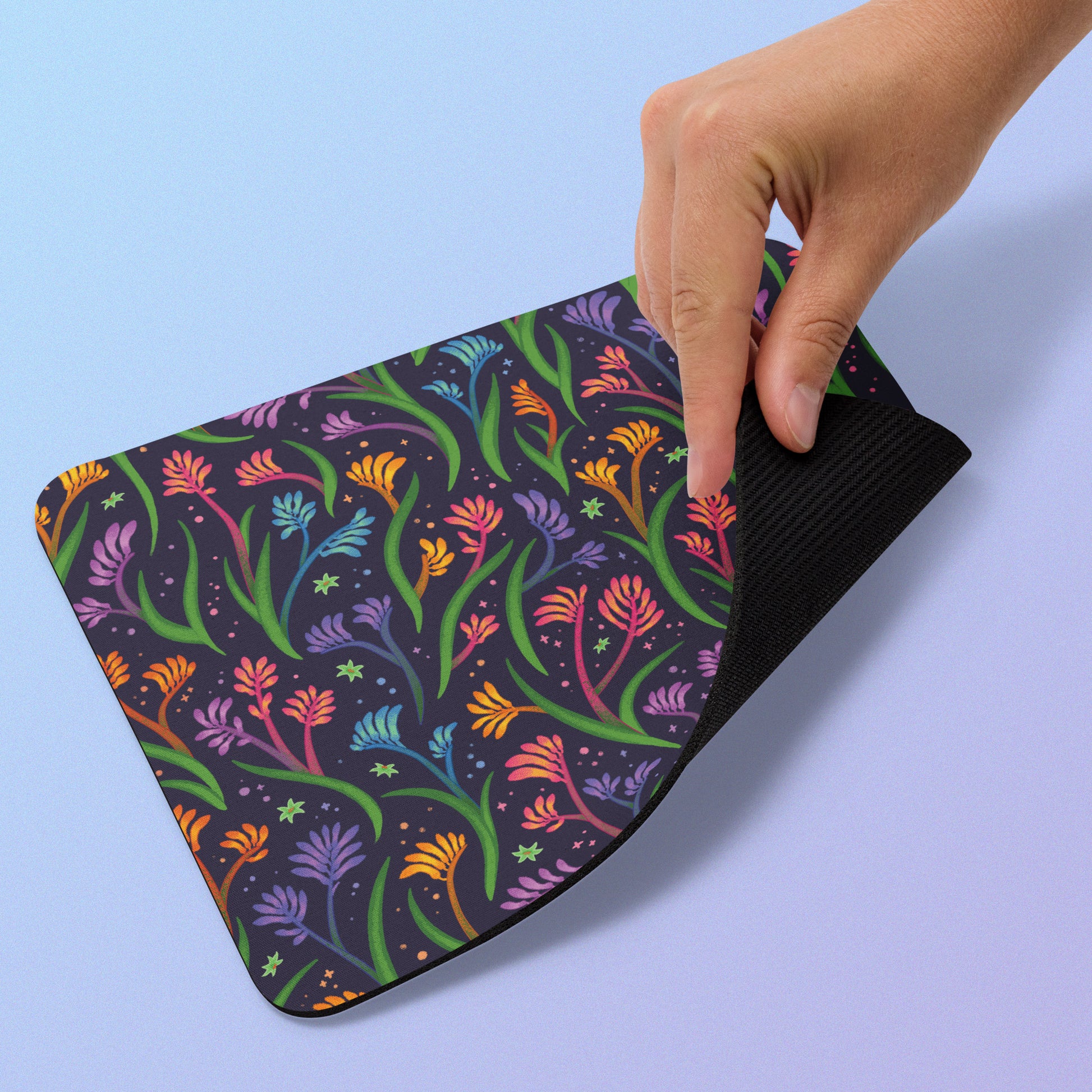 Colourful floral kangaroo paw mouse pad with a hand lifting the edge on a light blue background