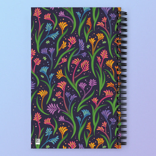 Spiral notebook with a colourful rainbow kangaroo paw flower pattern on a pink and purple gradient background.