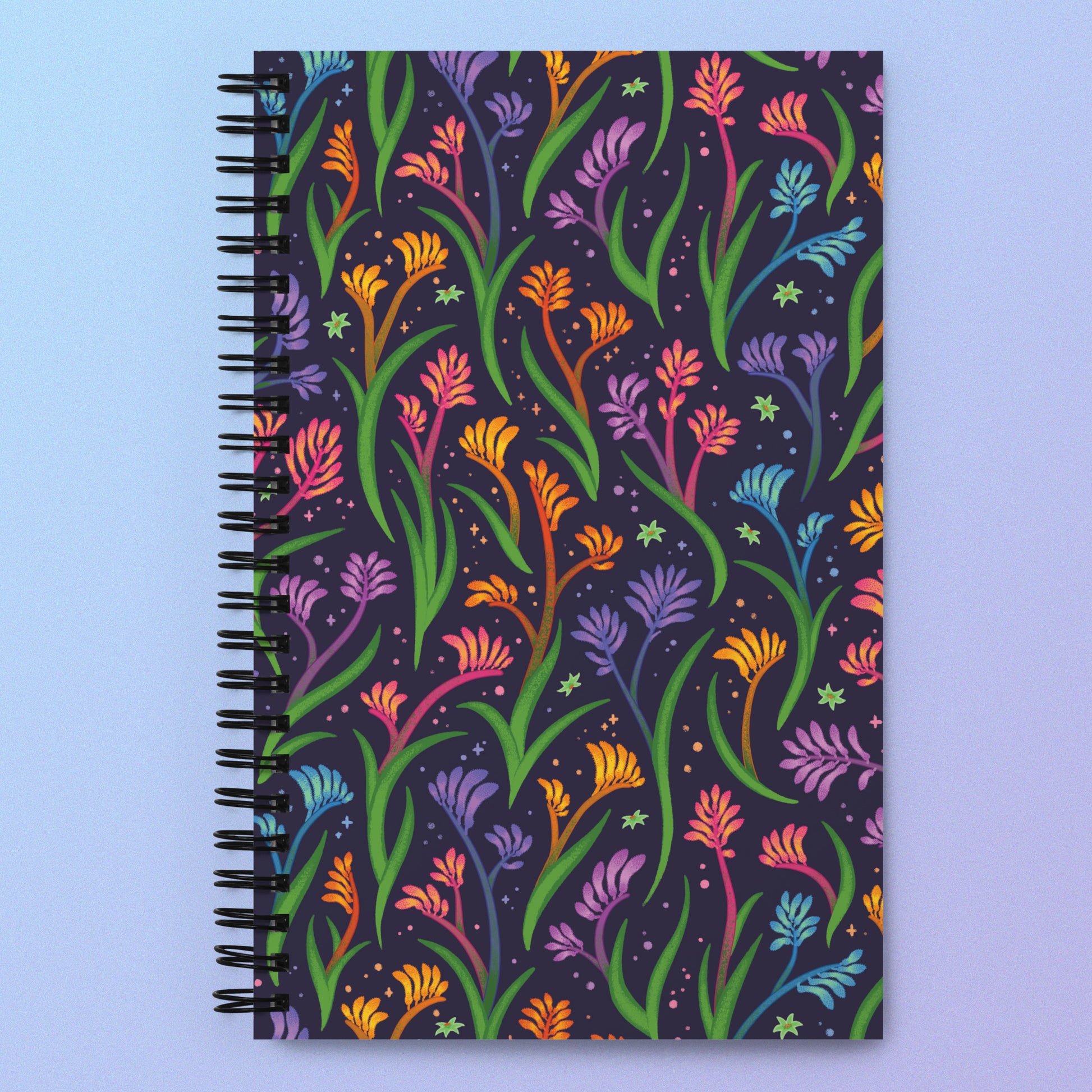 Spiral notebook with a colourful rainbow kangaroo paw flower pattern on a pink and purple gradient background.